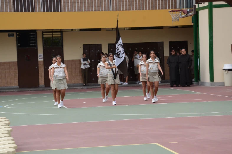 some pretty girls standing by a basketball court holding a black flag
