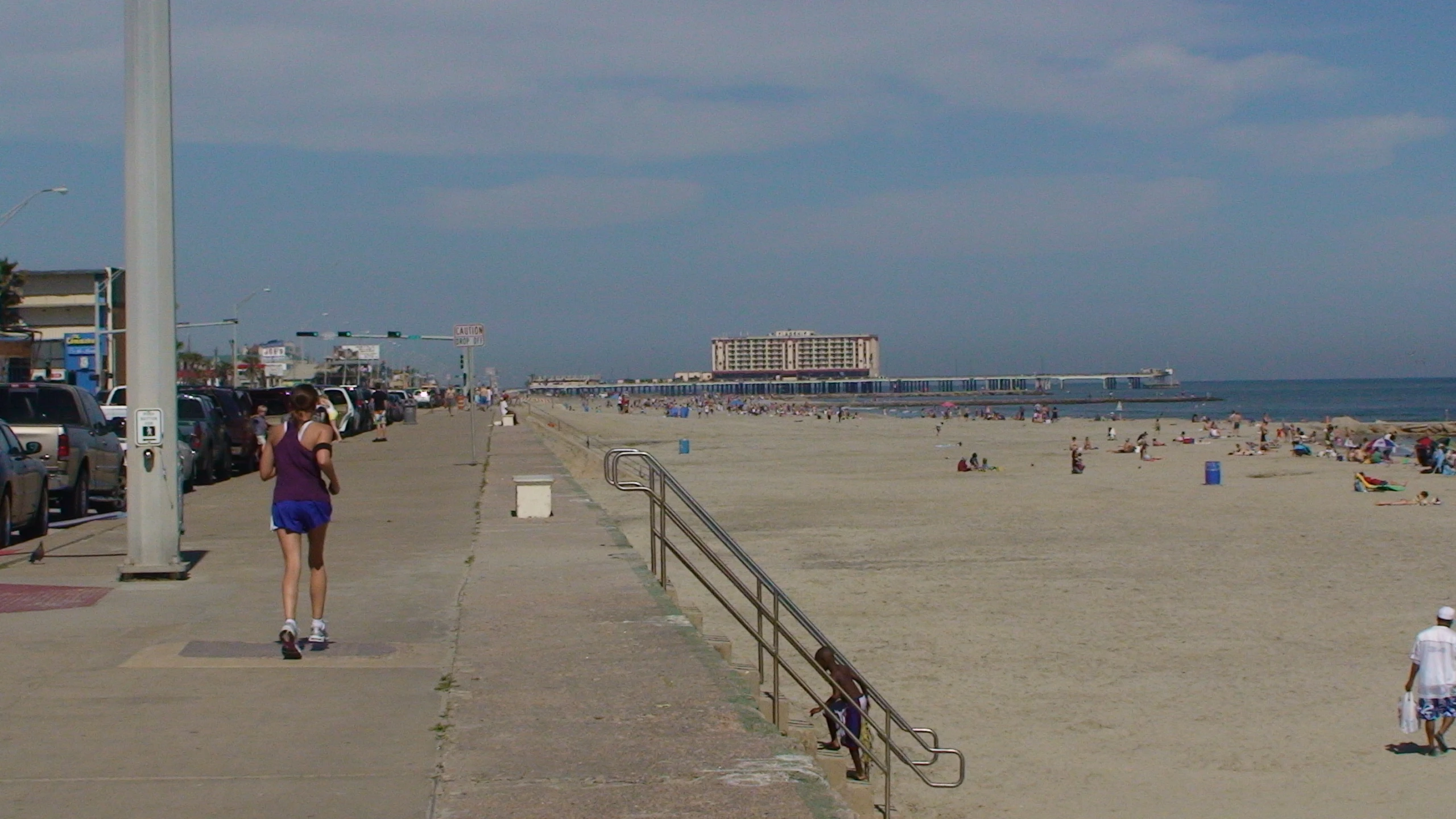 many people on the beach with a boardwalk and a building