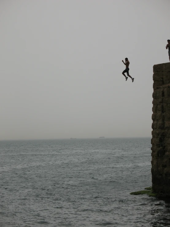 two people jumping off of a cliff into the water
