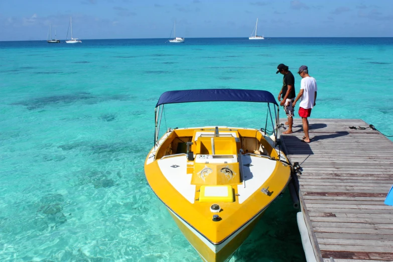 two people standing on the dock near a yellow boat