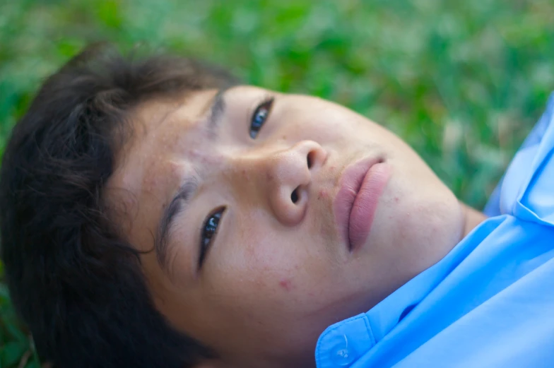 young man lying in grass and staring at camera