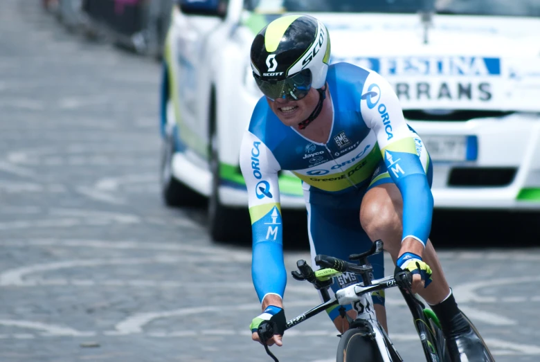 professional cyclist in bicycle racing next to white and green car