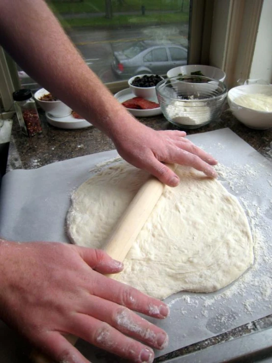 the hands of a man are rolling dough on a table