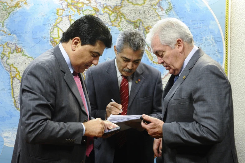 three men standing next to each other in front of a map