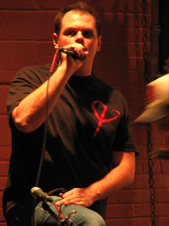 a man wearing a black t - shirt with the letter x on it, while holding a microphone