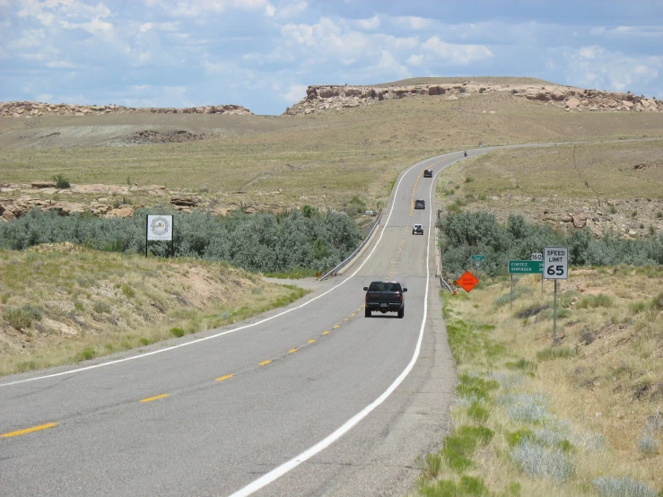 cars and trucks driving on a narrow road in the prairie