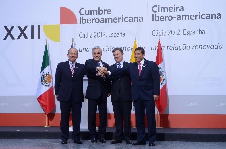 three men in suits posing with a ribbon while other men stand near the one