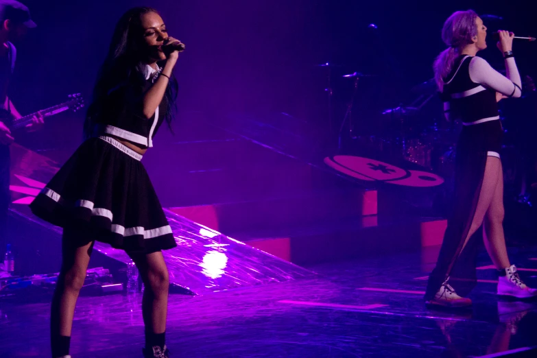 two girls singing on stage with bright purple lighting