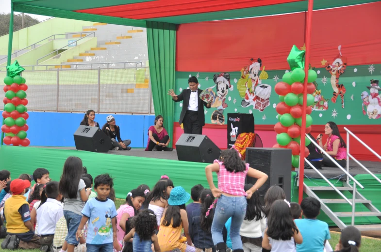 children are sitting on the stage, with an entertainer in the center