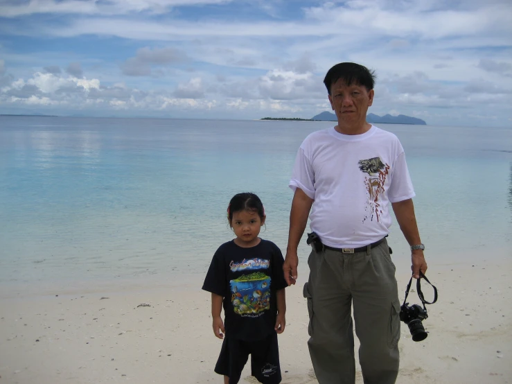 a man and a boy standing on the beach next to a body of water