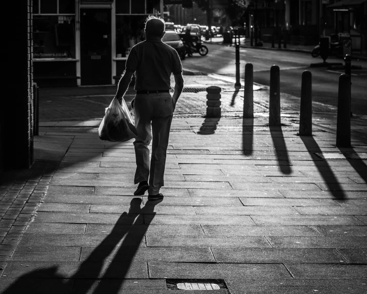 black and white image of man walking on sidewalk in city