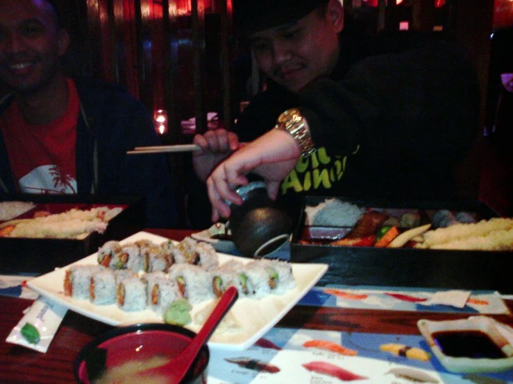 two men and a woman are eating sushi at a restaurant