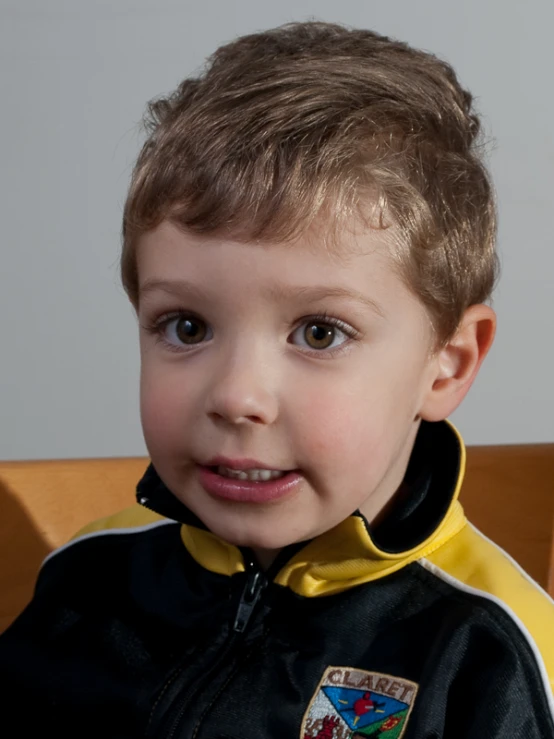 a boy with dark eyes wearing a yellow shirt and black jacket