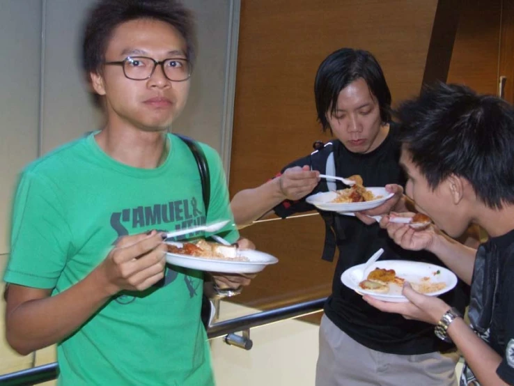 three guys eat food from plates in front of them