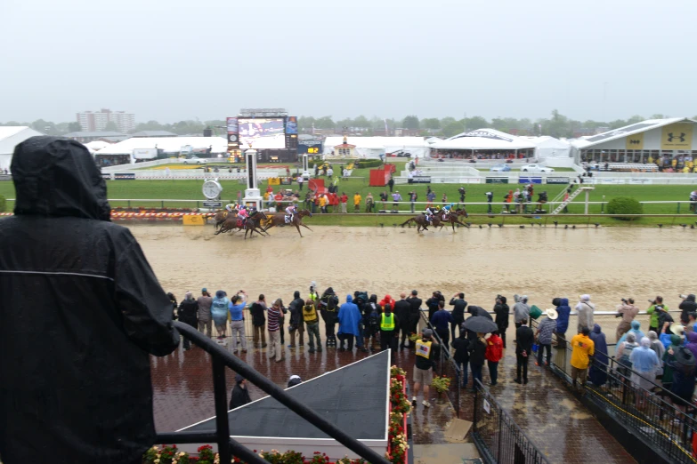 people in raincoats watching race horses and riders