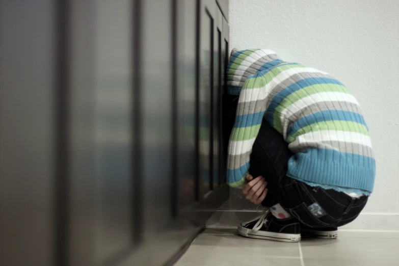 a young man is kneeling against the wall with his head on a cupboard