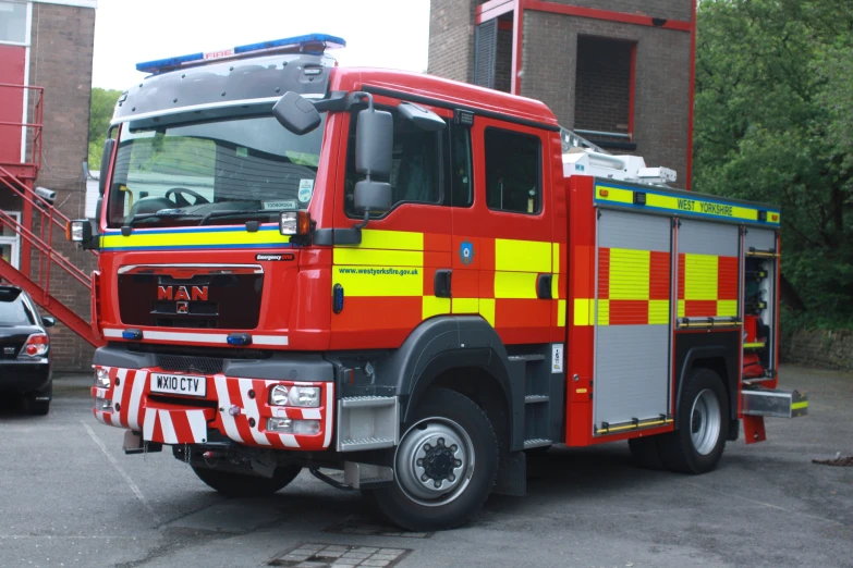 a red and yellow fire truck with ladder next to a brick building