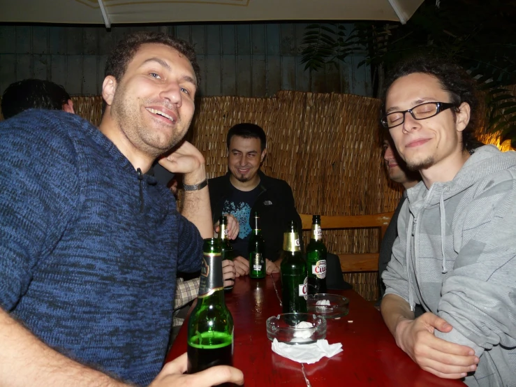 three men smiling with drinks on a red table