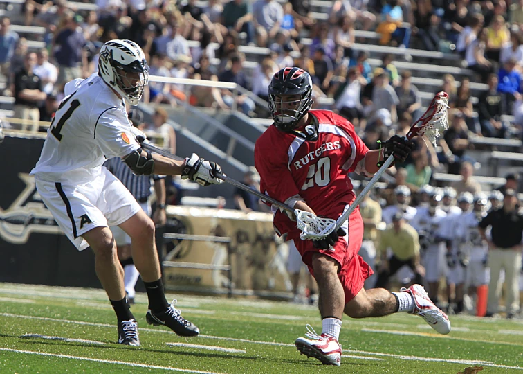 two players in action on the field, one holding a lacrosse racket