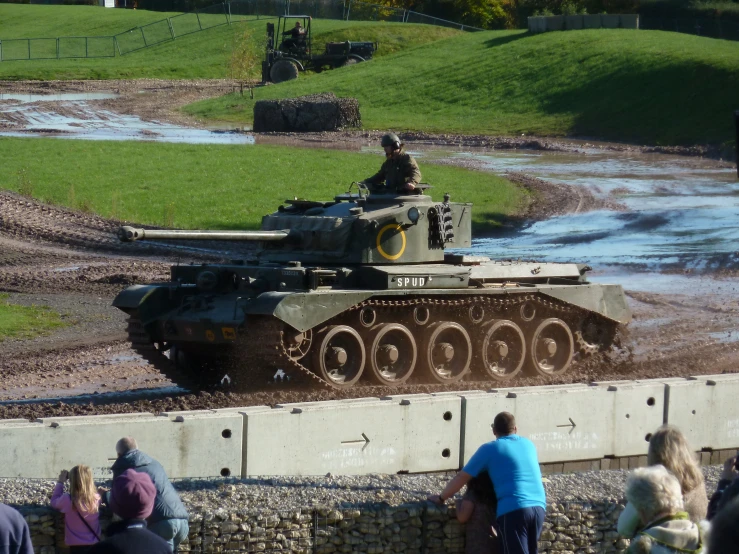 an army tank is parked near a wall in the middle of a grassy field