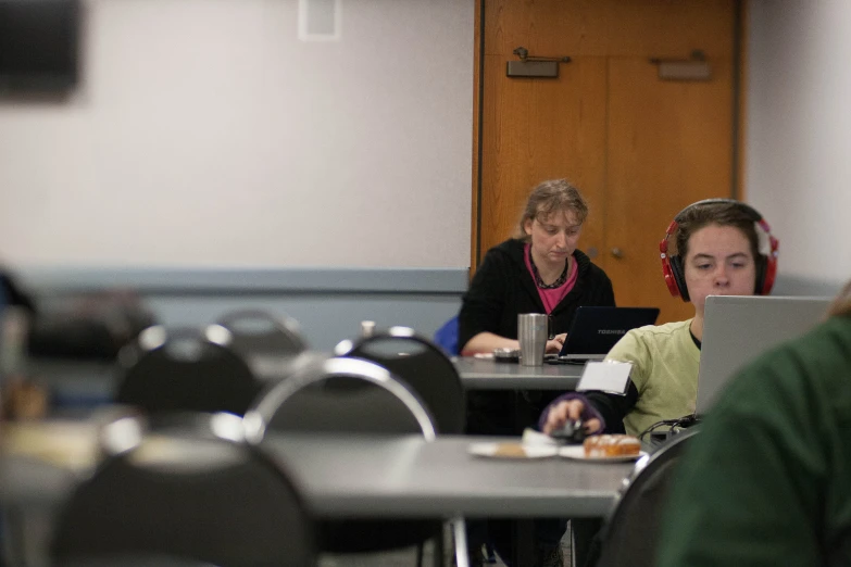 two women sitting in chairs at a table with laptops