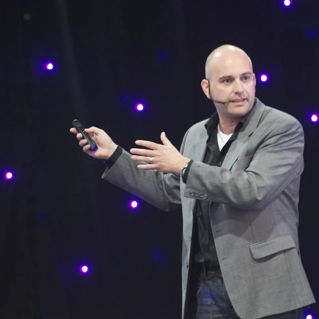 a bald man speaking while presenting at an event