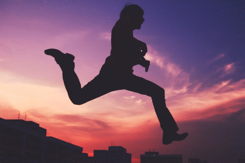 silhouette of a woman jumping in the air in front of sunset