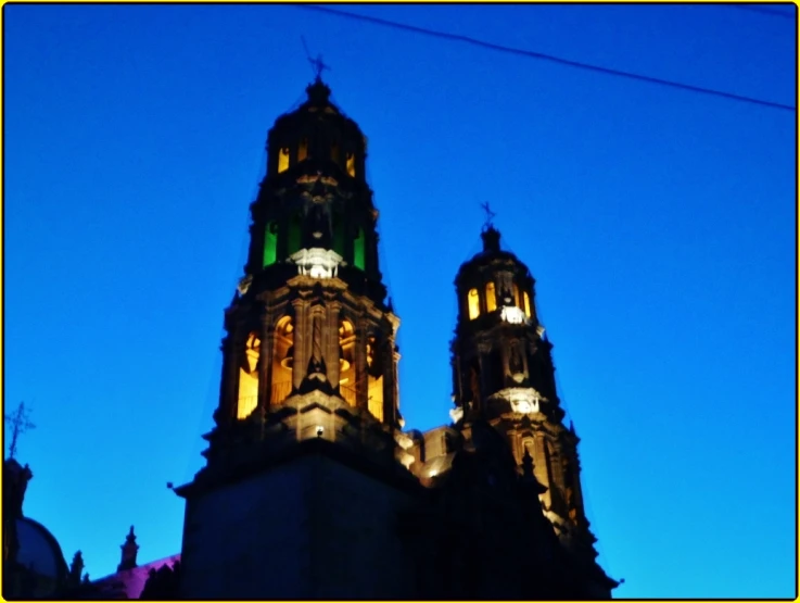 view at night from below, looking up to the tower of a building that is illuminated with bright lights