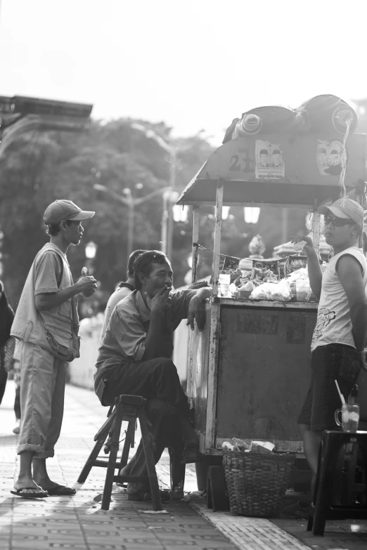 a woman selling food from a cart with two people standing by