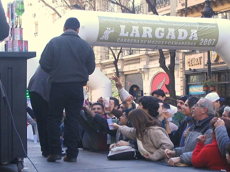 a man speaking on stage while lots of people sit near by