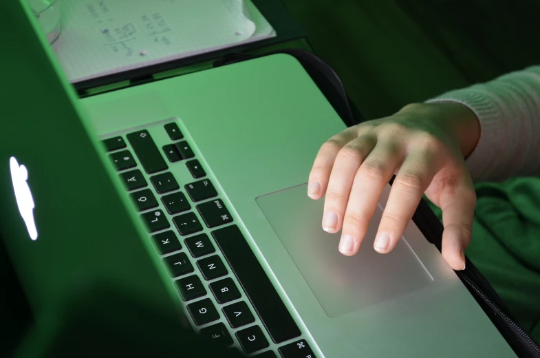 a person typing on a green laptop with their hand