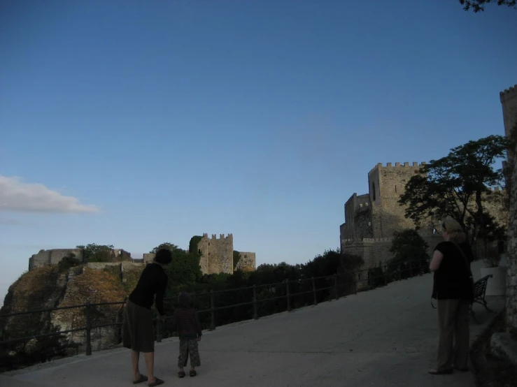 people looking at an old castle against a blue sky