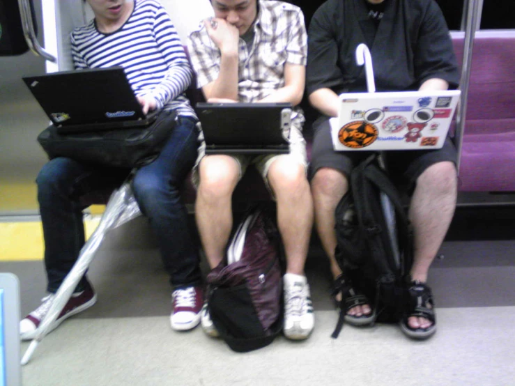 three guys with laptops sit on the subway train