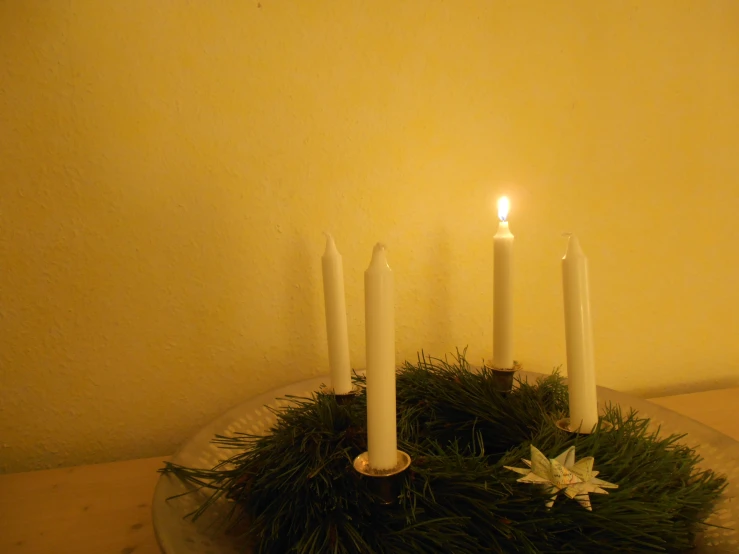three candles with greenery on top and one candle sticking out from between two candles