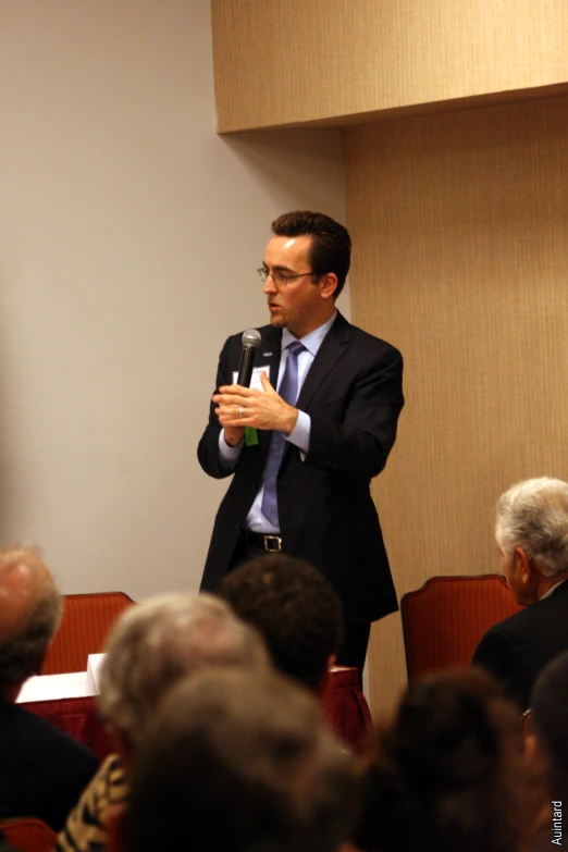 a man in a black jacket and tie standing behind a microphone