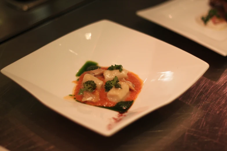 a square white plate with ravioli covered in red sauce