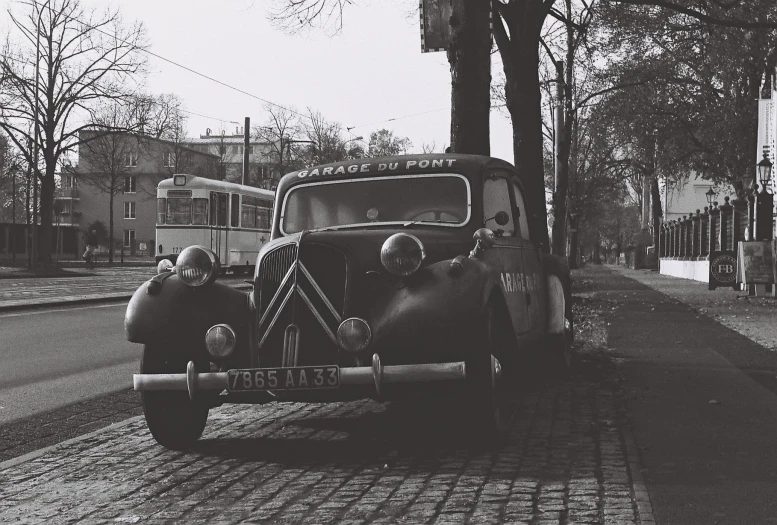 a black and white picture of an antique car parked next to a tree