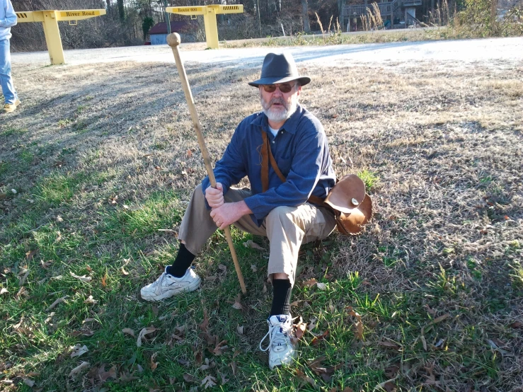 a man is sitting on the ground with his hat on and a shovel is leaning up against him