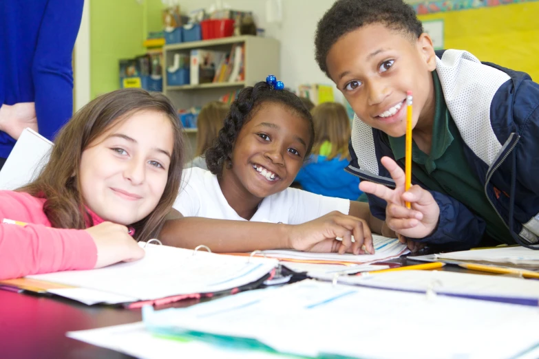 three children are posing for the camera in front of school work