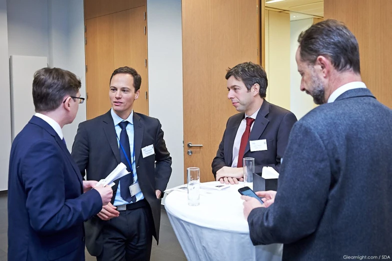 four men are standing in a room, discussing a meeting