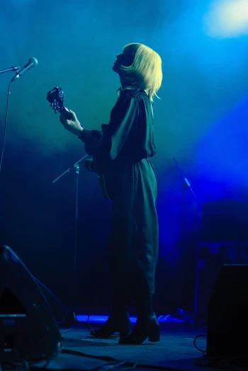 a woman playing guitar on stage with blue light