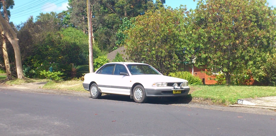 a white car parked next to a green tree