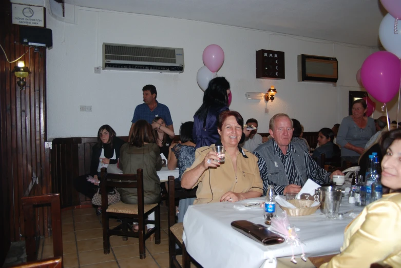 a group of people are sitting in a room with birthday balloons