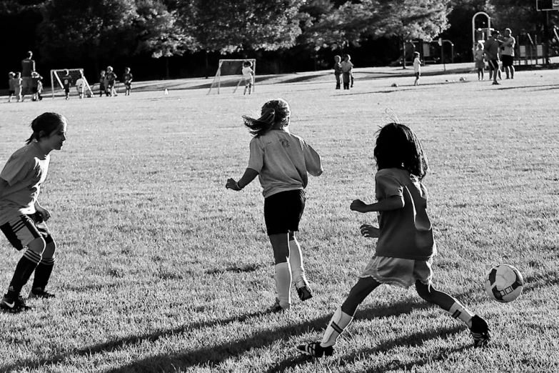 three children playing soccer while others watch