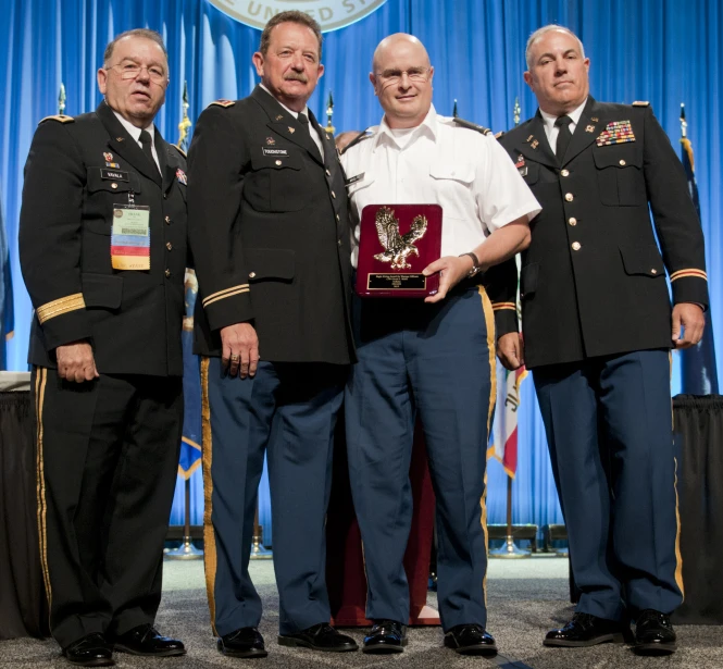 three military men standing with one holding up a plaque