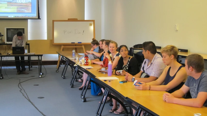 a group of students at a classroom table with a presentation screen in the background