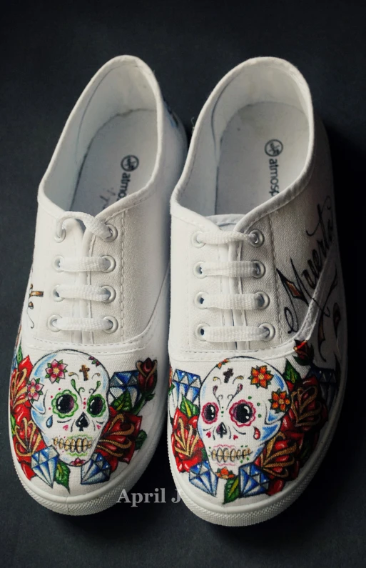a pair of white canvas shoes decorated with a sugar skull and flowers