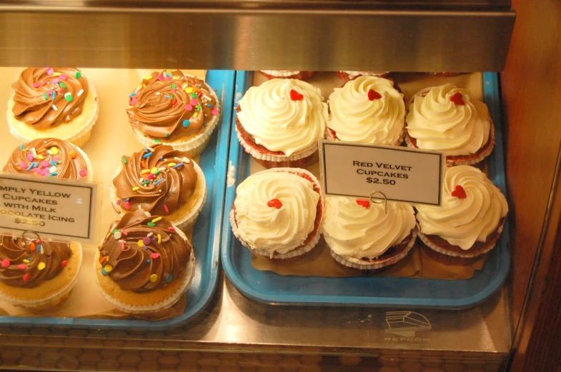 cupcakes and cakes in a display case for sale