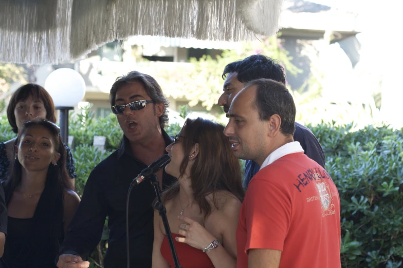 several people standing in front of a microphone while two women talk to the camera