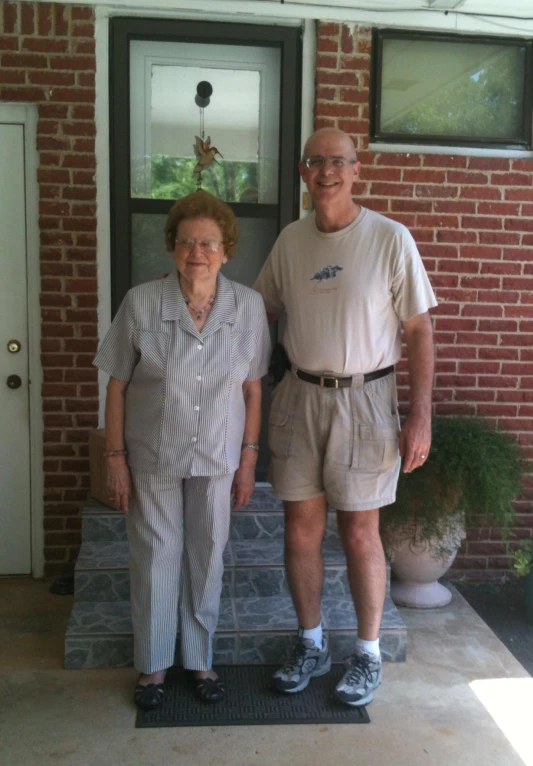 an older couple stand together outside their house